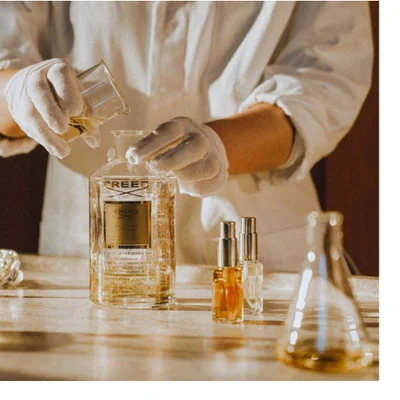 Hand holding a Creed Aventus Cologne perfume bottle with text reading CREED and AVENTUS COLOGNE