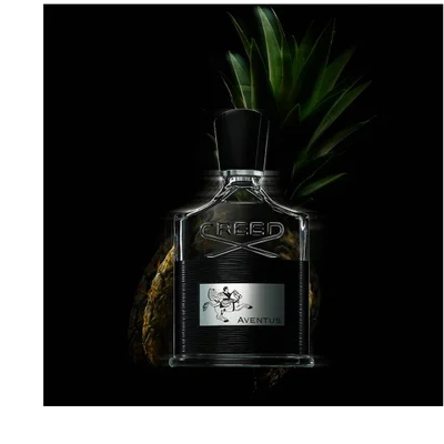A Creed Aventus perfume bottle is shown in front of a pineapple with the text CREED AVENTUS visible on the bottle.