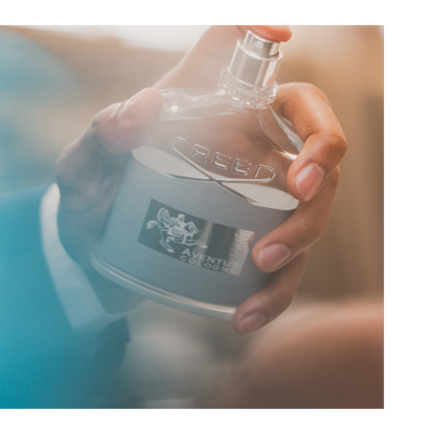 A hand holds a bottle of cologne with CREED AVENTUS COLOGNE text and a logo visible.