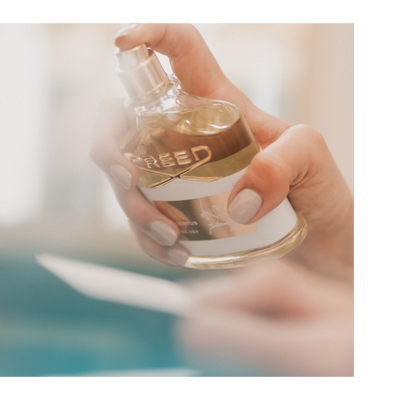 Hand holding a Creed Aventus Cologne perfume bottle with text reading CREED and AVENTUS COLOGNE