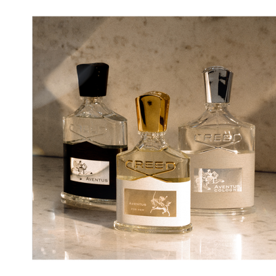 A photo shows three Creed perfume bottles, one dark liquid Aventus, one light liquid Aventus For Her, and one light liquid Aventus Cologne, with visible text including CREED, AVENUS, AVENUS FOR HER, AVENUS COLOGNE