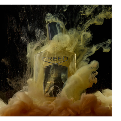 A Creed Royal Oud perfume bottle is surrounded by swirling yellow and brown liquid against a black background, with text on the bottle reading CREED ROYAL OUD DE PERE EN FILS DEPUIS FROM FATHER TO SON SINCE 100ML 3.3 FL.OZ.