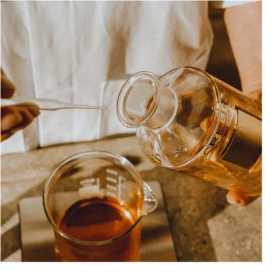 A Creed Royal Oud perfume bottle is surrounded by swirling yellow and brown liquid against a black background, with text on the bottle reading CREED ROYAL OUD DE PERE EN FILS DEPUIS FROM FATHER TO SON SINCE 100ML 3.3 FL.OZ.