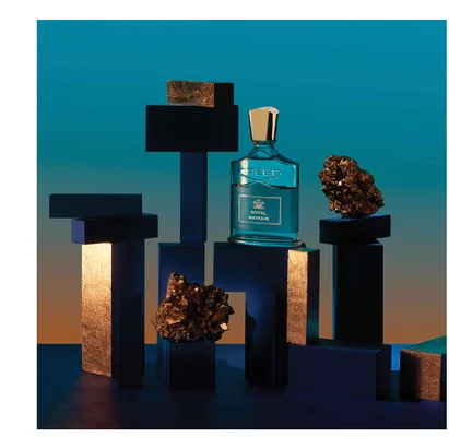 A bottle of Creed Royal Mayfair perfume is displayed among dark blocks and crystals with the text CREED ROYAL MAYFAIR visible on the label.