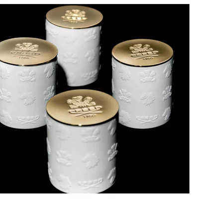 Four white ceramic containers with embossed patterns of crests, lions, and horses and gold lids featuring the text CREED 1760.