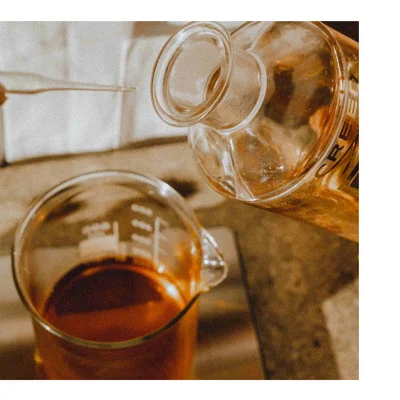 Liquid is poured from a bottle with the text CREE into a beaker containing dark liquid while a pipette is held above.