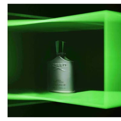 A Creed Green Irish Tweed fragrance bottle is illuminated by green light and features the text CREED GREEN IRISH TWEED DE PERE EN FILS DEPUIS 1760 FROM FATHER TO SON SINCE 1760 100 ML 3.33 FL. OZ.