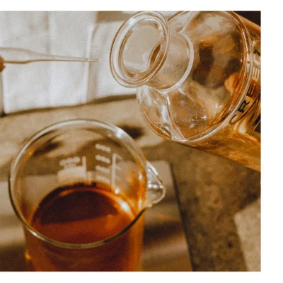 Liquid is poured from a bottle with the text CREE into a beaker containing dark liquid while a pipette is held above.