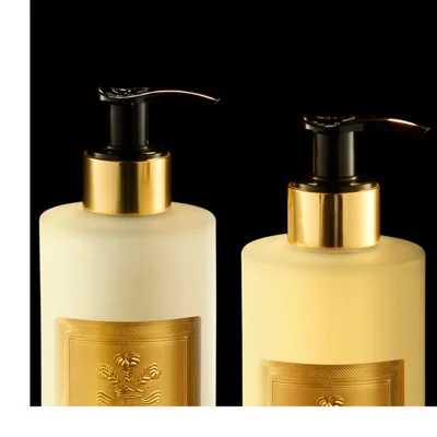 A red Creed Carmina perfume bottle with a gold cap, a beige hand cream tube, two beige pump bottles for hand and body wash and lotion, and a round beige soap bar are displayed on a dark reflective surface with golden liquid effects; visible text on the items includes Creed, 1760, Carmina, Hand Cream, Creme Mains, Hand & Body Wash, Lavant Liquide, Hand & Body Lotion, and Lait Riche.