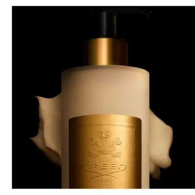 A frosted white lotion bottle with a black pump and gold neck is featured, with a golden embossed label on the front and a swirl of light-colored lotion behind it, displaying the text CREED 1760.