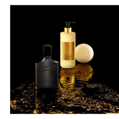 A dark fragrance bottle, a cream pump bottle, and a spherical cream soap are displayed on a black surface with golden shimmering liquid; the fragrance bottle reads CREED GREEN IRISH TWEED, the pump bottle reads CREED 1760 GREEN IRISH TWEED HAND & BODY WASH SAVON LIQUIDE MAINS ET CORPS, and the soap reads CREED 1760.