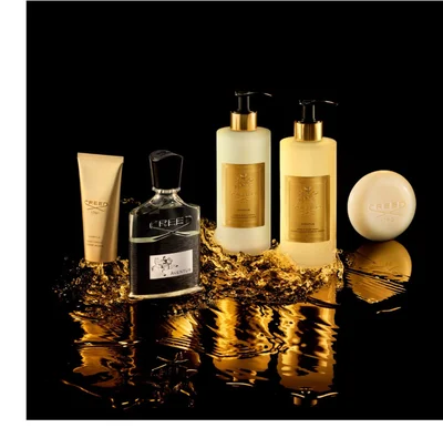 A dark brown perfume bottle with a gold cap is surrounded by swirling white smoke against a black background, displaying the words CREED, a gold crest, and OUD ZARIAN on its front.