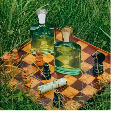 Creed Original Vetiver and Wild Vetiver bottles on chessboard with chess pieces in grass.