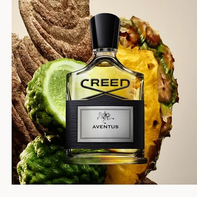 Creed Aventus bottle with pineapple, red berries, vanilla, and woods arranged on a clean white background.